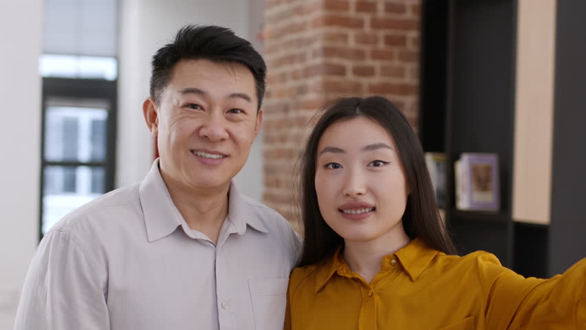 Family blog. Happy asian married man and woman recording video message on smartphone to social media, standing together at home interior, camera pov portrait | Shutterstock HD Video #1111772435