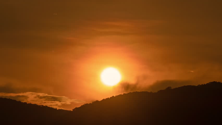Time lapse of the sun rising over hills that are covered with clouds, in the style of smokey background.