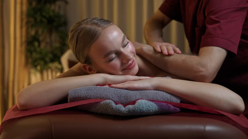Professional masseur makes a relaxing back massage to a young woman, pretty female enjoy a massage, warm lighting, spa treatments. | Shutterstock HD Video #1111773927