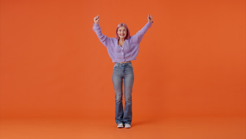 Full length portrait of attractive female dressed in casual sweater and jeans saying wow, claping hands and making yes gesture over orange studio background. Concept of success and lifestyles.