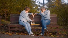 Front view of two mature people dressed in denim attire playing chess on park bench. Lovely caucasian couple doing favorite hobby together on fresh air. Background of autumn trees and fallen leaves. - Powered by Shutterstock - Get 15% off with code: PIKWIZARD15