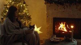Woman in cozy sweater caressing cute cat on laps and relaxing at cozy burning fireplace in christmas eve in festive room. Atmospheric christmas eve footage. Pet and winter holiday
 - Powered by Shutterstock - Get 15% off with code: PIKWIZARD15