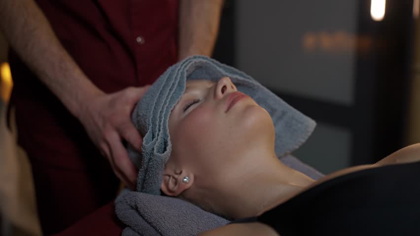 Handheld, pro masseur makes a relaxing head massage to a young woman, beautiful female enjoy a massage, warm lighting, spa treatments. | Shutterstock HD Video #1111775769