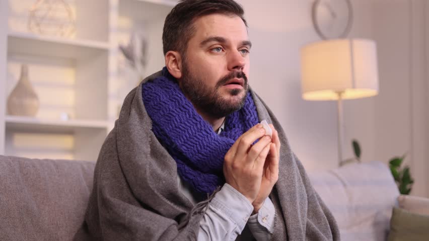 Sick unhealthy mature man sitting on couch with warm scarf coughing sneezing and having severe headache temperature at home Sad tired guy getting flu virus symptom at cold season | Shutterstock HD Video #1111778945