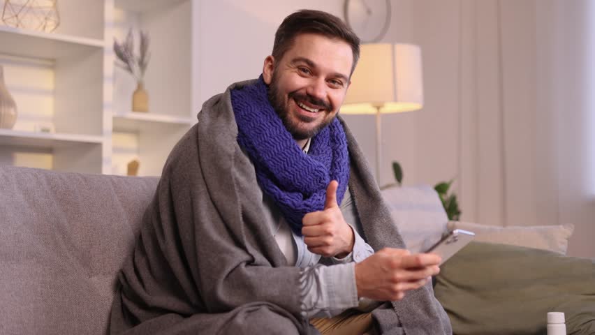 Sick man under the blanket coughing sneezing having severe headache temperature when mentioned useful medical app service or site looking at camera with thumbs up at home Help service concept | Shutterstock HD Video #1111778955