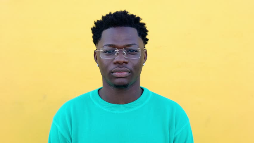 Close-up portrait of young adult african man smiling at camera over yellow background. Front view headshot of joyful black guy feeling positive outdoors. Royalty-Free Stock Footage #1111779033