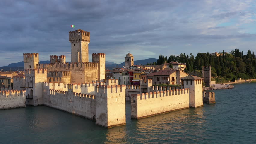 Historical part of the city of Sirmione on Lake Garda in Italy, slow motion shot by drone. Scaliger Castle of the city of Sirmione 4K video on drone. Cumulus clouds at sunrise Sirmione. Royalty-Free Stock Footage #1111780355