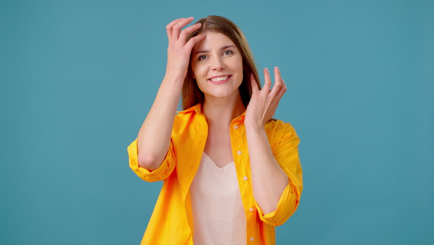 Pretty woman fixes hair and freshens makeup with graceful motion. Young female takes brief pause to ensure presentable look against blue background | Shutterstock HD Video #1111780663
