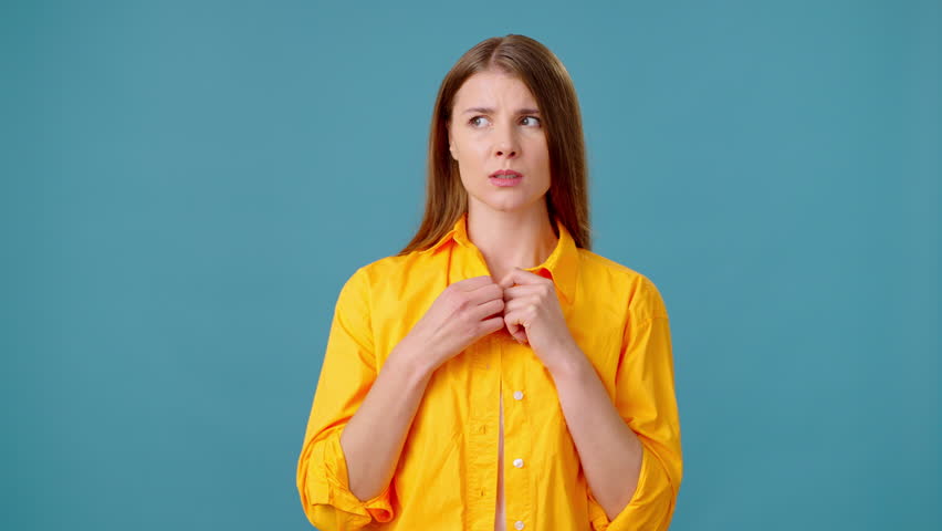 Young woman bites nails consumed with anxious thoughts. Nervous female glances around with wary look standing in studio with blue background | Shutterstock HD Video #1111780695