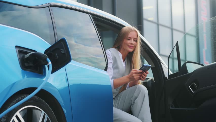 Beautiful woman connects plug to electric car in parking lot. Eco friendly alternative energy green environment concept. | Shutterstock HD Video #1111781923