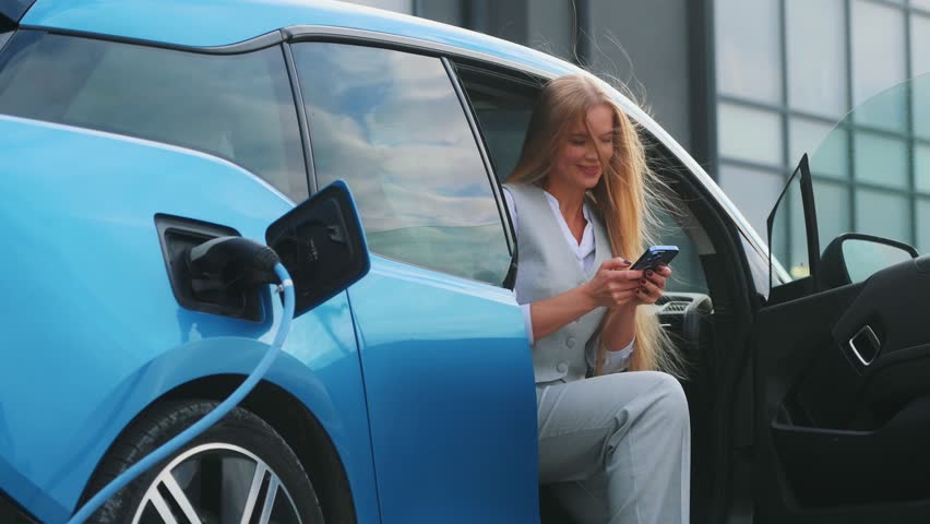 Beautiful woman connects plug to electric car in parking lot. Eco friendly alternative energy green environment concept. | Shutterstock HD Video #1111781969