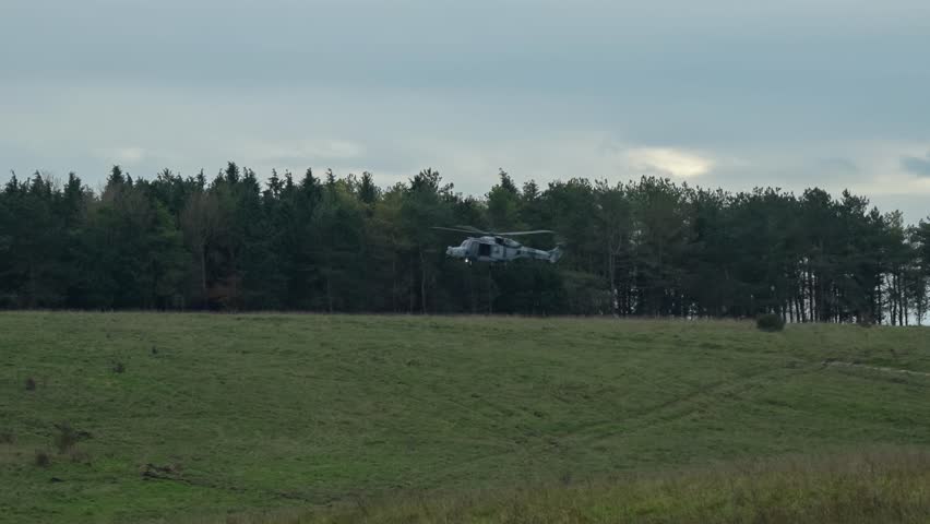 British army AgustaWestland AW159 Wildcat AH1 helicopter hovering by woodland