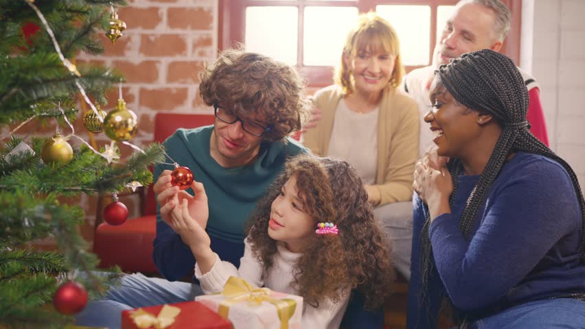 Multi-ethnic family and young daughter decorate Christmas tree in house. Young little daughter feeling happy and excited to celebrate holiday Christmas Thanksgiving party with parents together at home | Shutterstock HD Video #1111786633