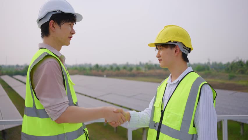 Young engineer making handshake, work with photovoltaic panel system. Attractive technician worker working on roof inspect and check solar cell panels equipment box at solar cell field during sunset. | Shutterstock HD Video #1111786695