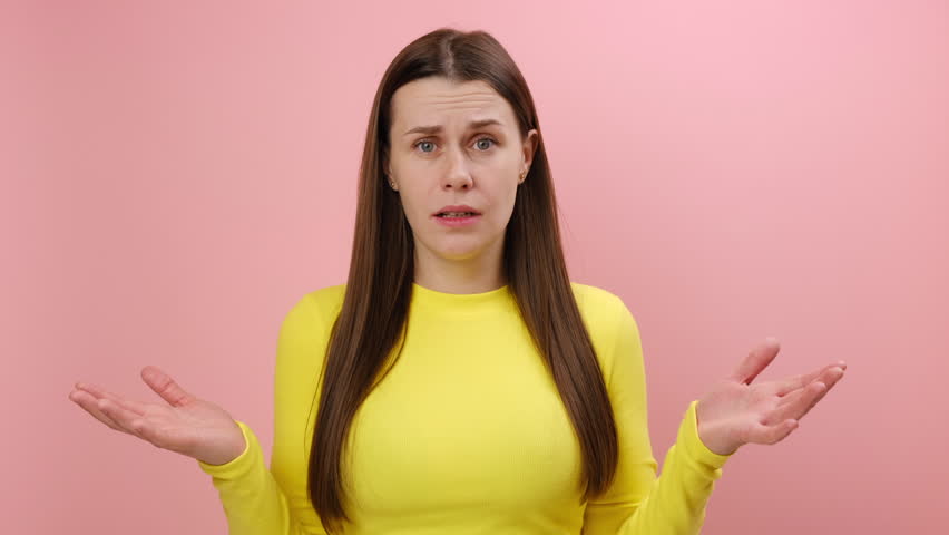 Irritated indignant young woman wearing yellow sweater raising hands in anger and shouting why how, what do you want, quarreling, looking at camera, posing isolated over pink background wall in studio | Shutterstock HD Video #1111786761