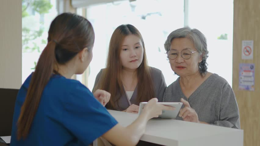 In the clinic at the Reception Desk, Asian nurse talking with a mother and her daughter at counter in hospital. She is typing on her tablet, Mother and daughter made a doctor's appointment. | Shutterstock HD Video #1111786977