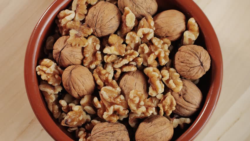 Mix of walnuts rotating in red plate top view. Walnut in shell, walnut without shell. Peeled nuts. Healthy snacks. Product rich in minerals and vitamins.