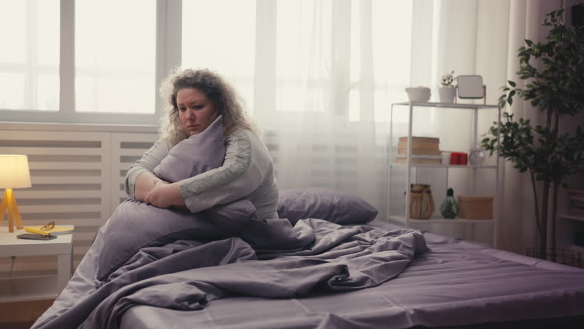 Lonely overweight woman sitting on bed, hugging pillow, marriage crisis breakup Royalty-Free Stock Footage #1111792015