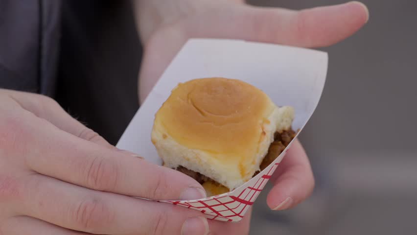 This close up video shows anonymous hands picking up a bbq slider sandwich.