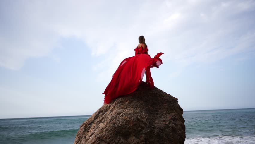 woman sea red dress. Woman with long hair on a sunny seashore in a red flowing dress, back view, silk fabric waving in the wind. Against the backdrop of the blue sky on the seashore. Royalty-Free Stock Footage #1111792345