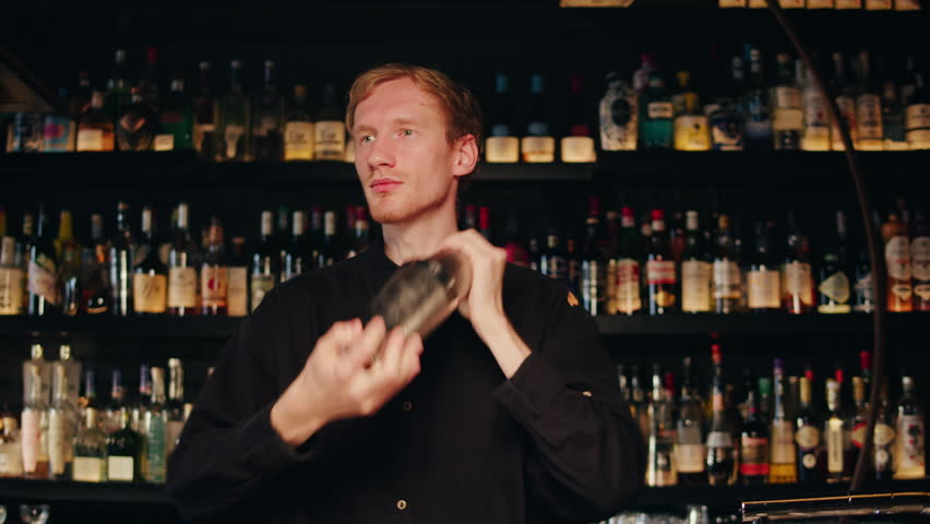 Young bartender doing a cocktail with shaker in the bar. Man making alcohol cocktail behind the bar counter close up | Shutterstock HD Video #1111793891