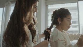 Young loving mother braiding hair of little daughter as she drinking juice and eating cookies in the morning at home - Powered by Shutterstock - Get 15% off with code: PIKWIZARD15