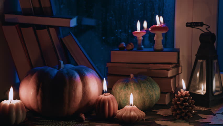 Perfect hygge autumn ambience. Stack of paper books, candles near rainy window.