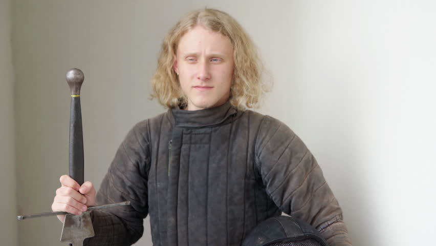 Portrait of a calm young teen dressed historical medieval fencing armor with a long sharp sword.