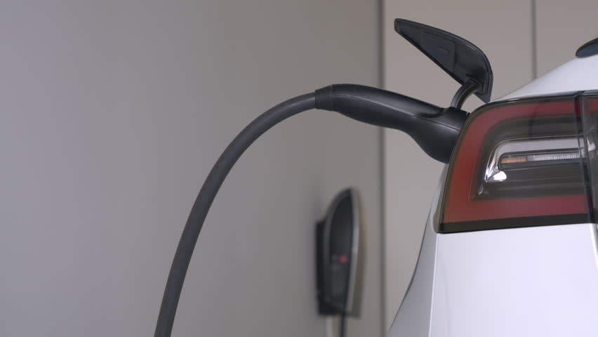 CLOSE UP: White electric car plugged into a charging station in home garage. Black power cord connected to BEV for powering the engine battery. Zero emission alternative for modern transportation. | Shutterstock HD Video #1111797615