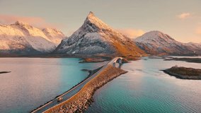 Aerial view of Fredvang bridge, car, sea and snowy mountains at sunset in Lofoten Islands, Norway. Landscape with beautiful road, water, rocks in snow, sky with pink clouds. Top view from drone - Powered by Shutterstock - Get 15% off with code: PIKWIZARD15