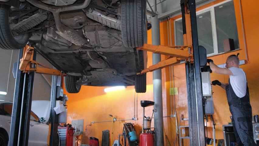 A mechanic working on a car in a car service. Professional repairman under the car. Modern car workshop | Shutterstock HD Video #1111800665