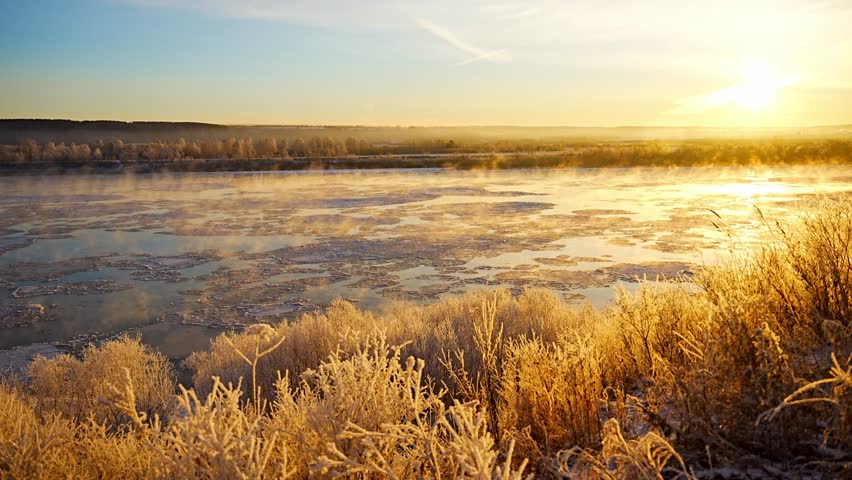 Cold winter landscape with trees covered with frost snow, river with flowing ices, fog and sunrise over horizon. Extreme low temperature weather in Siberia. High quality 4k footage