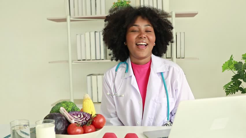 African American female nutritionist sits and talks giving information and benefits of a healthy nutrition plan to a patient stored on a laptop for clinical work. | Shutterstock HD Video #1111808311