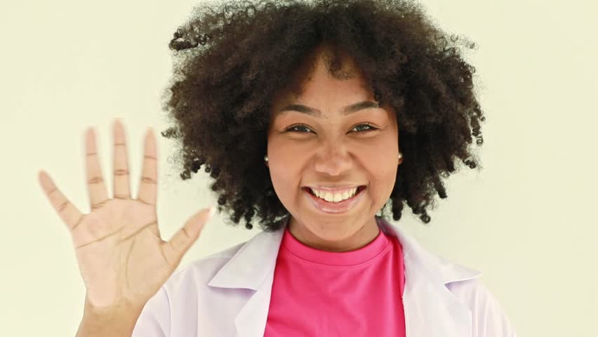 Cute African American female nutritionist sitting on a desk, smiling and raising her hand in greeting, sitting on a desk in a hospital office. | Shutterstock HD Video #1111808339