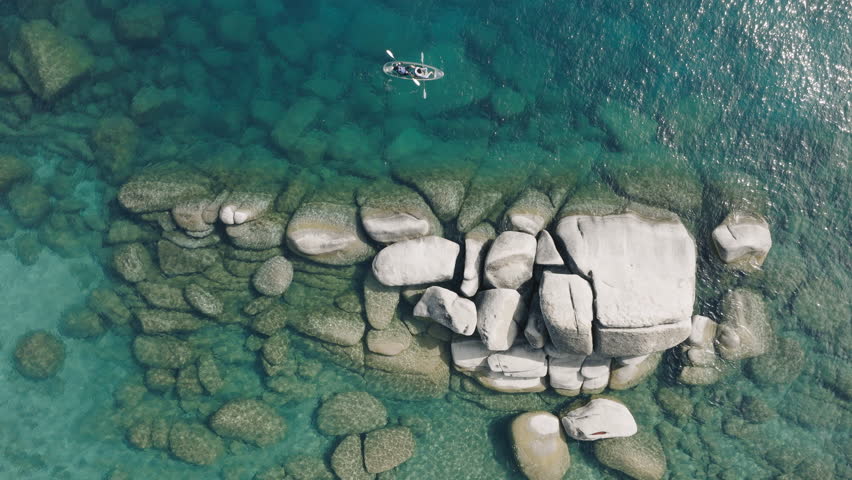 Drone view tourists on weekend adventure paddling in clear kayak. Water sport activity leisure. Sunny light refracting on clear water. couple kayaking together in pristine blue lagoon in lake Tahoe 4K