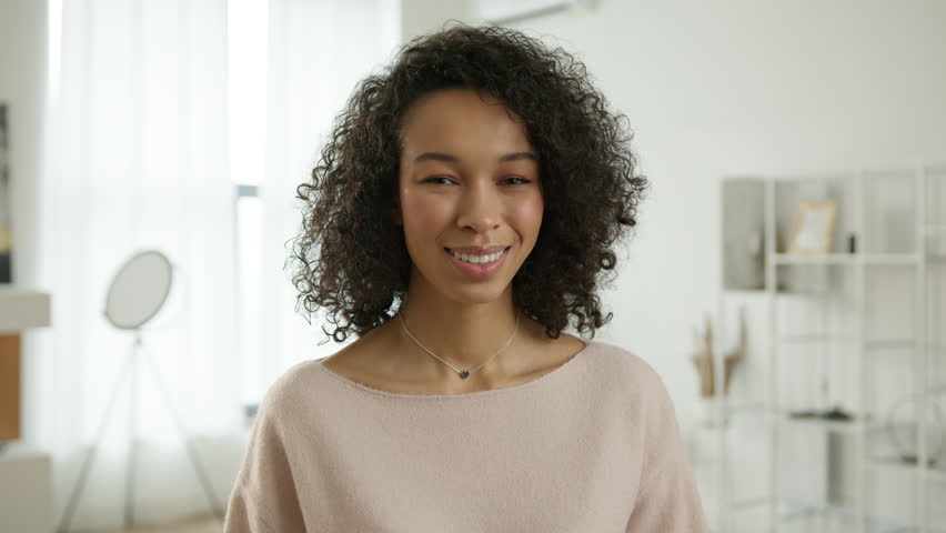 Portrait happy millennial casual professional lady with white teeth looking at camera. Pretty face woman of color posing indoors. Confident smiling young adult bi racial woman standing at modern home | Shutterstock HD Video #1111809585