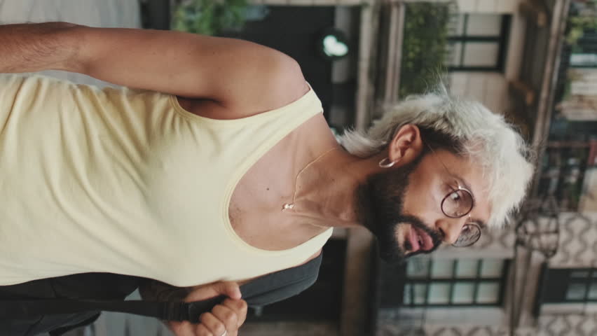 Vertical video, Handsome guy with blond hair wearing glasses walks through city and points out landmarks