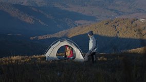 African American man sets up tent on top of mountain. Woman sits in tent and drinks cup of hot tea. Diverse tourist couple on camping vacation. Multiethnic family hiking on beautiful mountain hill. - Powered by Shutterstock - Get 15% off with code: PIKWIZARD15