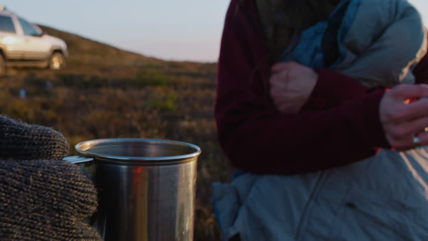Close up of young Caucasian woman clinking cups with African American man. Multiethnic couple of hikers stands on top of hill, talks and looks at sunset. Tourists enjoy view on vacation in mountains. | Shutterstock HD Video #1111815105