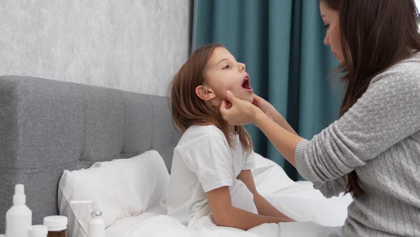 Woman spraying throat spray in daughter mouth, close-up. A mother treats her sick child  throat by sprinkling medications with a spray bottle, 4k Royalty-Free Stock Footage #1111815363