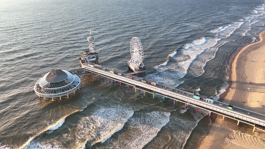 The Pier sky view, The Hague, Netherlands. A pier with amusement rides. An aerial view of the wide beach and waves. Seascape from a drone during sunset. A sandy seashore. The sea and the shore. 