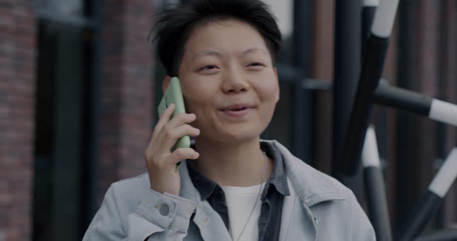 Portrait of cheerful Asian person speaking on mobile phone standing in busy city street. Cellphone communication and urban lifestyle concept. | Shutterstock HD Video #1111822065