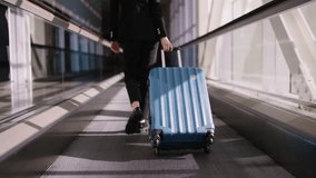 Caucasian young woman in black business suit confidently pulling a blue suitcase on an airport moving walkway, symbolizing efficiency and pace of modern business travel - Powered by Shutterstock - Get 15% off with code: PIKWIZARD15