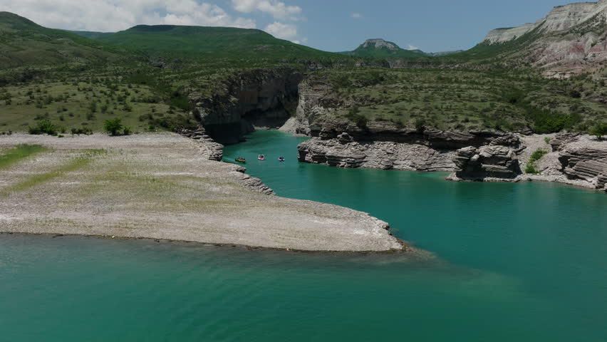 A river with boats in it. A majestic river winds through the rugged mountain landscape, adorned with colorful boats, as the endless sky and fluffy clouds reflect upon its glistening waters, inviting