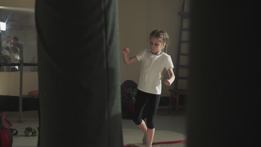 Kid kicks punching bag jumping with teammates in gym. Active little girl exercises with equipment during group lesson in sports club slow motion | Shutterstock HD Video #1111829347