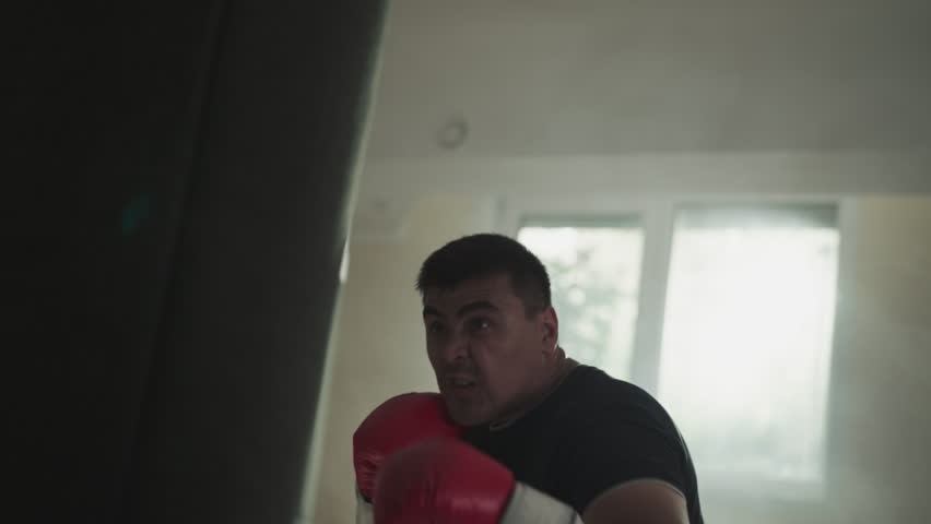 Strong man hits punching bag by arms with gloves in gym. Martial arts master punches equipment in boxing club slow motion. Combat training performance | Shutterstock HD Video #1111829397