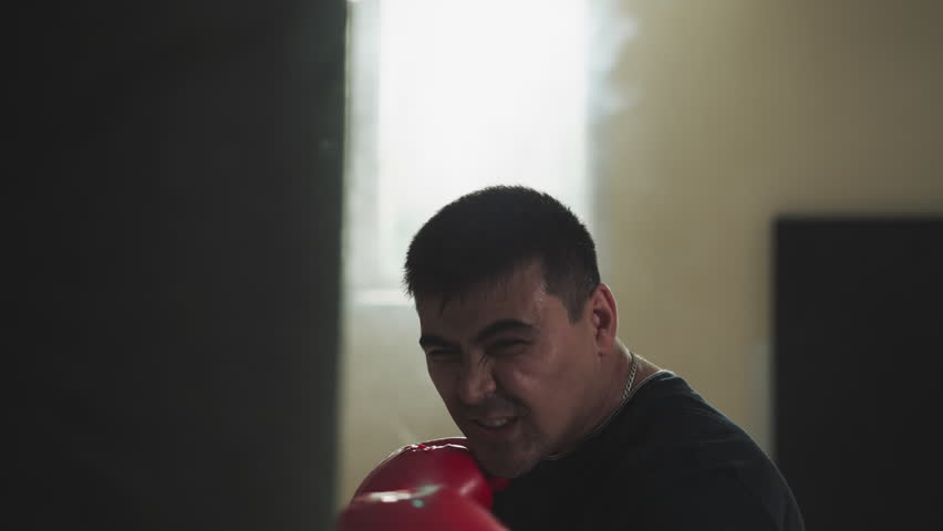 Boxer punches heavy bag in sports club. Professional sportsman does exercises with fighting equipment in gym slow motion. Martial arts champion | Shutterstock HD Video #1111829399