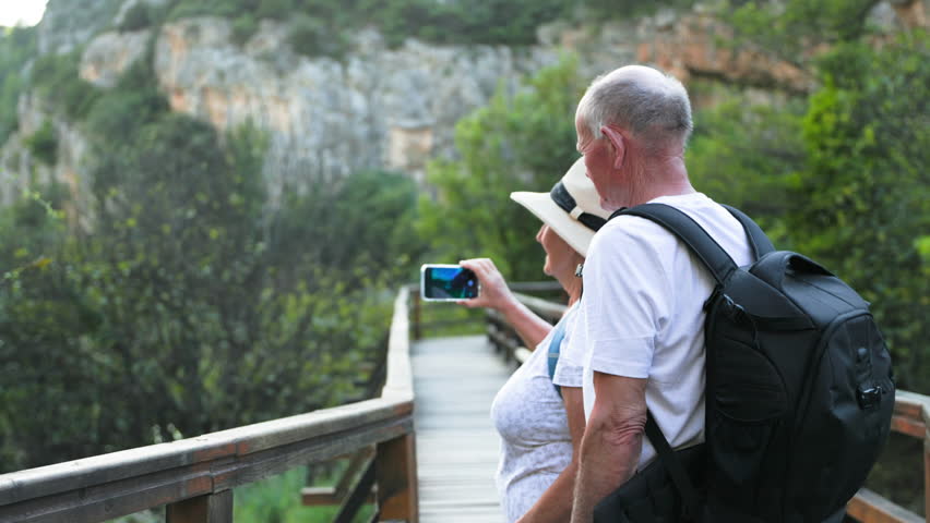happy old man and elderly woman having fun while walking in the park and taking selfie while standing on a bridge in park