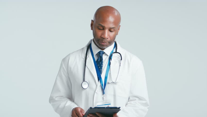 Studio portrait of mature male doctor wearing white coat holding digital tablet against white background - shot in slow motion | Shutterstock HD Video #1111830459