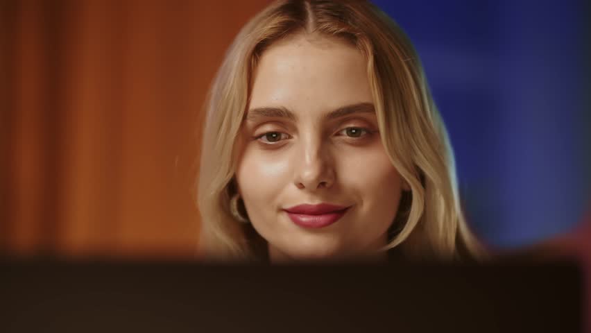 A young pretty blonde girl with a confident and satisfied gaze looks at the screen of a computer monitor or laptop. A smiling business lady reads good news about job, feels herself the mistress and | Shutterstock HD Video #1111832739